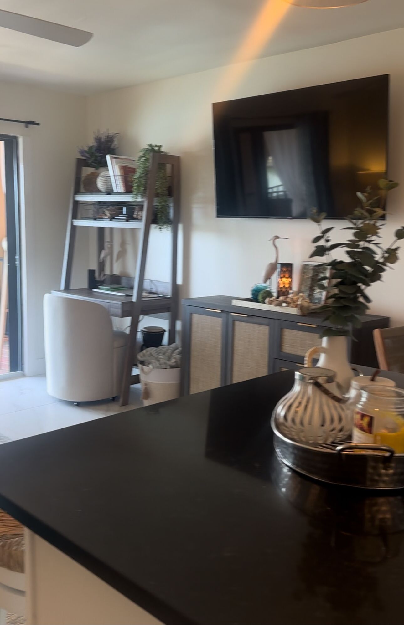 A modern kitchen with a black countertop, a white chair, a wooden ladder, and a TV mounted on the wall.