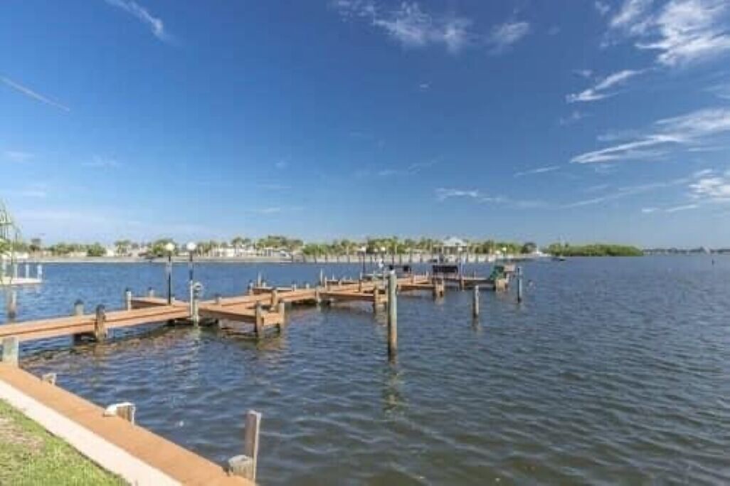Un quai au bord de l’eau, avec des jetées en bois s’avançant dans une eau calme, le tout baigné d’un ciel bleu clair.