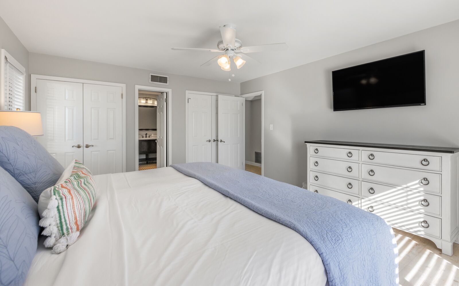 A bedroom with a bed, a dresser, a ceiling fan, and a TV.