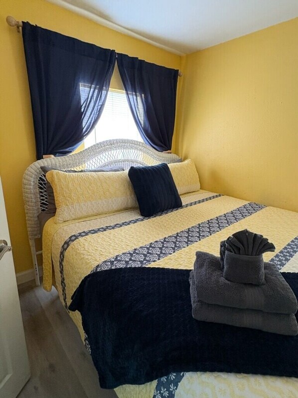 Una cama con una colcha estampada, una almohada azul oscuro y una toalla doblada al lado.
