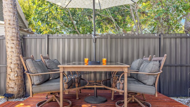 Un patio con una mesa, dos sillas, un árbol y una valla de madera.