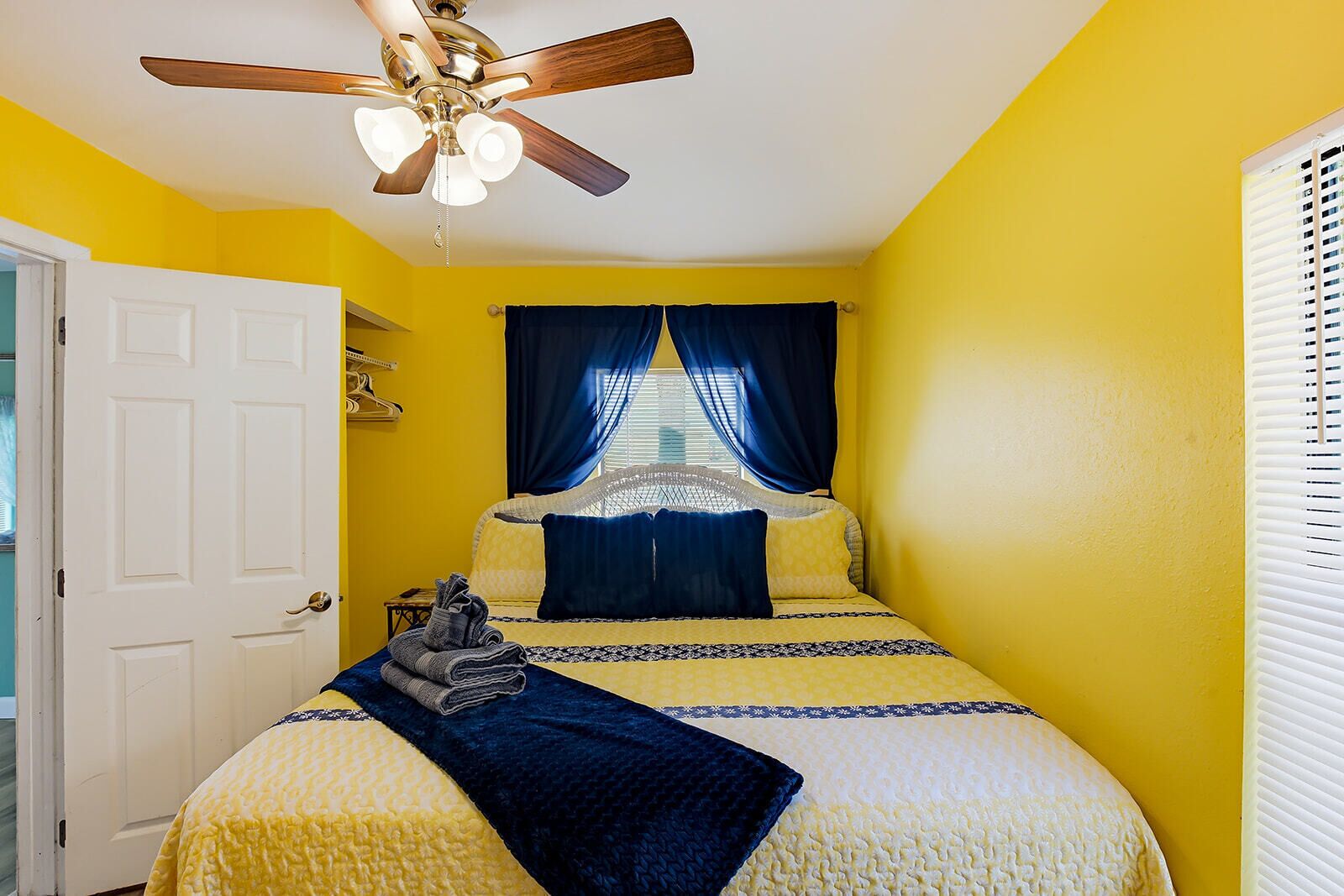 A bedroom with a bed, a ceiling fan, a window with curtains, and a door.