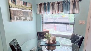 Un área de comedor con una mesa de vidrio rodeada por sillas de cuero, una ventana con persianas y un cuadro colgado en la pared.