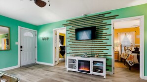 Una sala de estar con un televisor instalado en un panel de madera, una mesa de centro de vidrio y una chimenea.