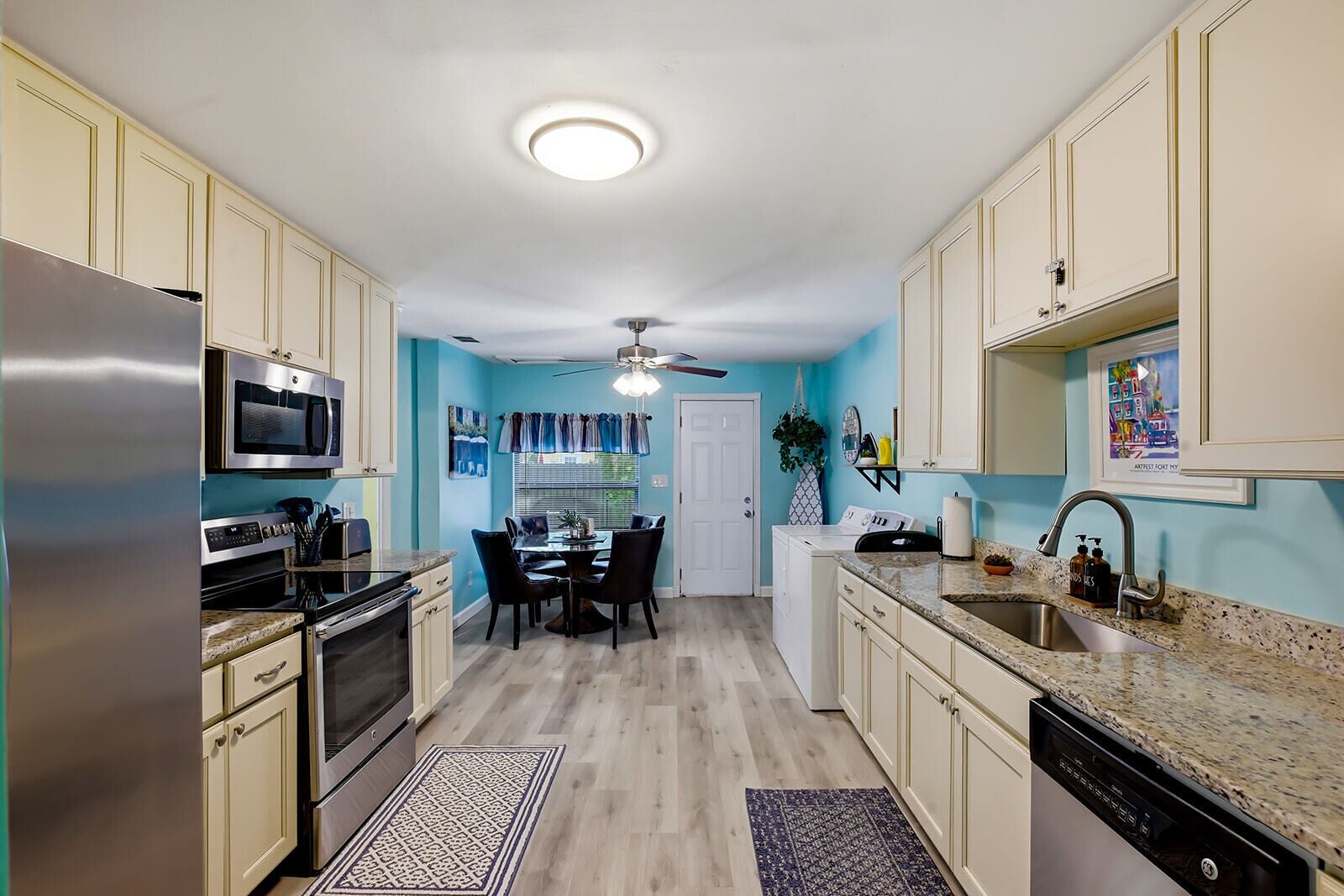 A kitchen with a dining area, stainless steel appliances, a ceiling fan, and light blue walls.