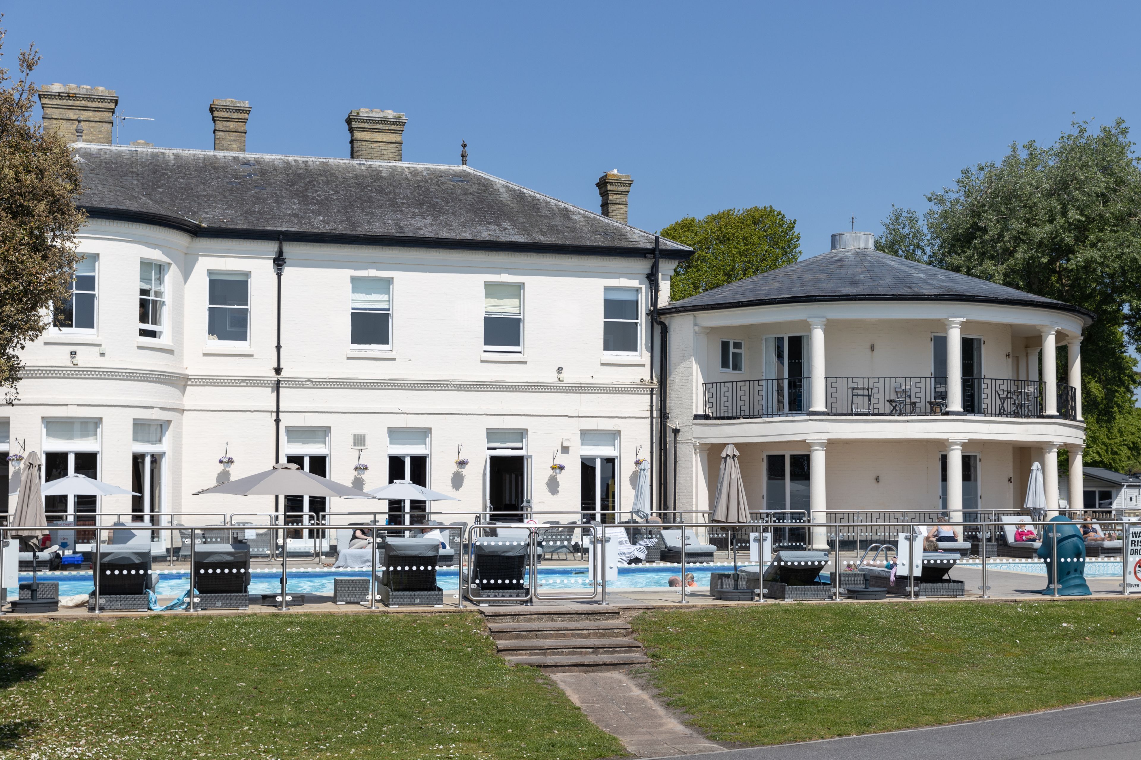 A two-story building with a swimming pool, outdoor seating, and a covered area.