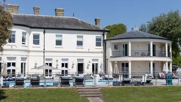 A two-story building with a swimming pool, outdoor seating, and a covered area.