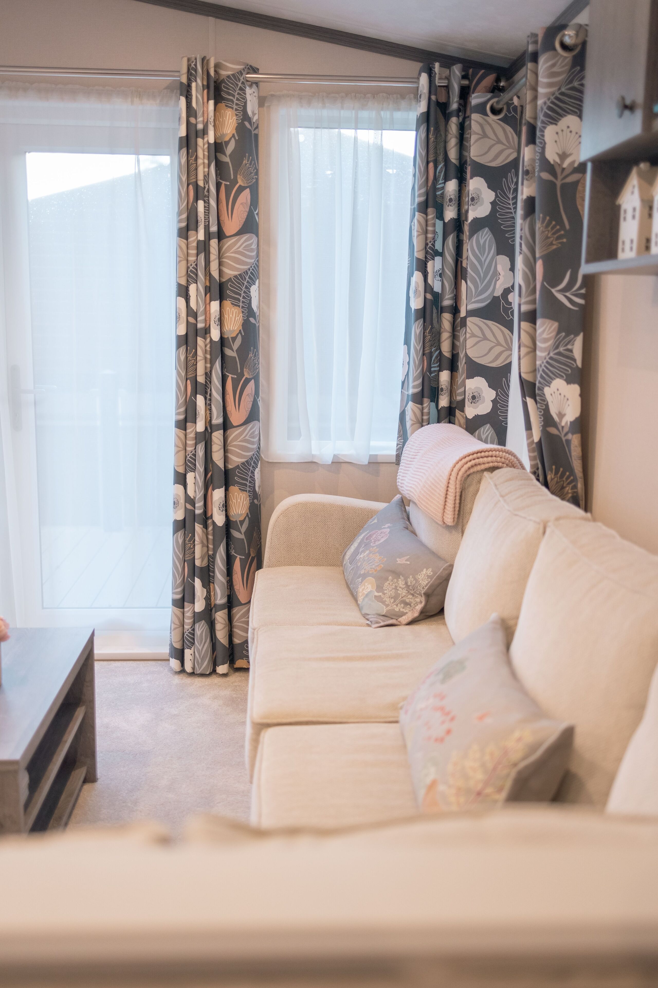 Un salon chaleureux avec un canapé beige, des rideaux à motifs floraux et une petite table.
