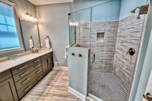 Un bagno moderno con doccia vetrata, un mobile lavabo con specchio e una finestra che lascia entrare luce naturale.