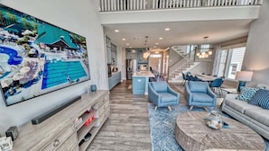 A spacious living room with a large TV, blue chairs, a round coffee table, and a staircase leading to an upper level. - Bayside * 4BR Luxury House (Selbyville)