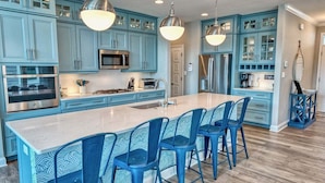 A kitchen with blue cabinets, stainless steel appliances, and a central island with bar stools. - Bayside * 4BR Luxury House (Selbyville)
