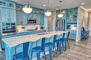 A kitchen with blue cabinets, stainless steel appliances, and a central island with bar stools. - Bayside * 4BR Luxury House (Selbyville)