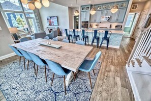 A modern kitchen with blue cabinets, a dining area with a wooden table and blue chairs, and a large window providing natural light.