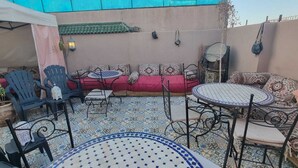 An outdoor patio with a red sofa, black chairs, a round table, and patterned floor tiles. - Riad Nouhal  (Marrakech)