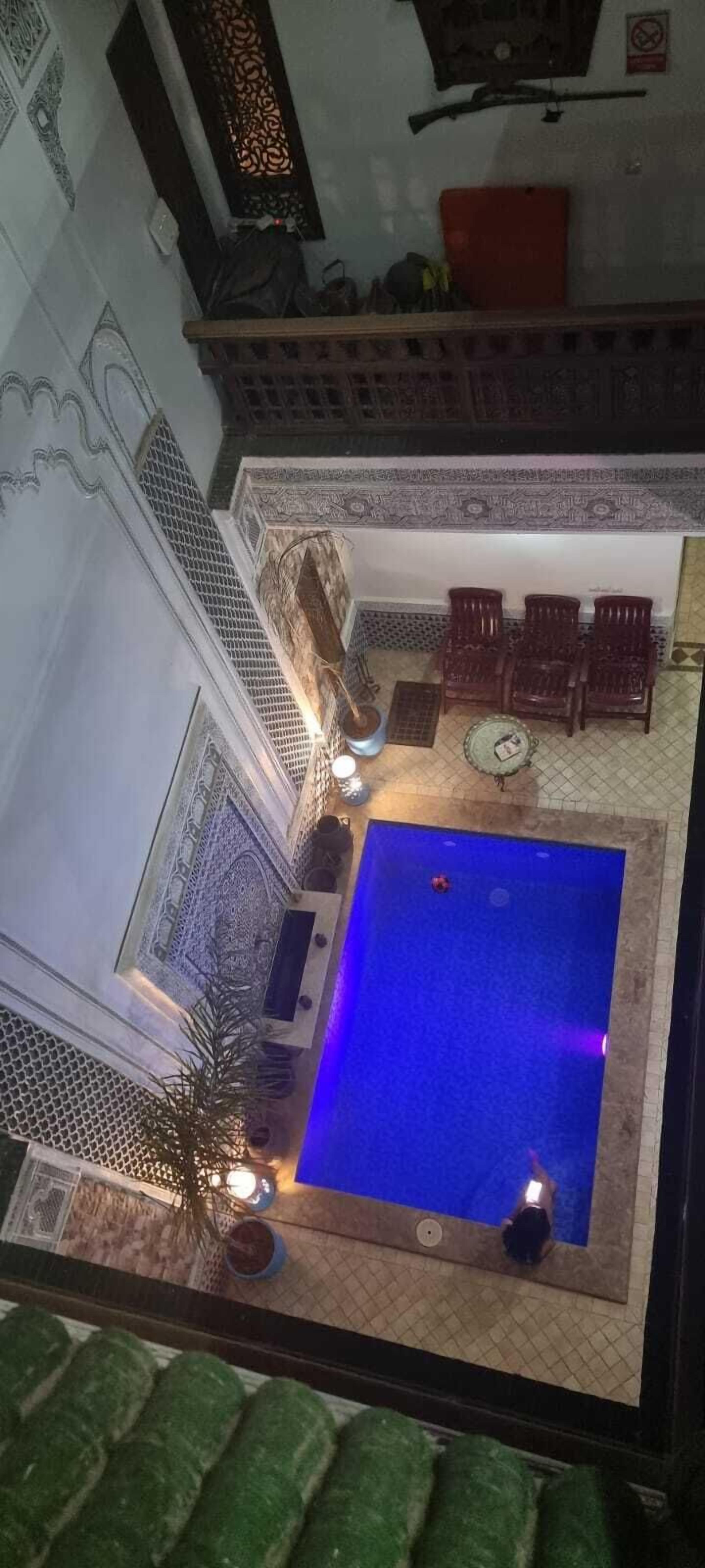 Una piscina al terrat amb una font d'aigua blava, envoltada de detalls arquitectònics ornamentals i una zona de seients amb mobiliari de fusta.
