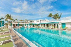 A pool area with lounge chairs and umbrellas, a building with multiple floors and balconies, and palm trees. - Tranquil Retreat ~ Waterfront Home, 37' Dock, Cabana Club! (Key Largo)