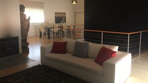A modern living room with a white sofa, red and grey cushions, a black rug, and a dining area with a cityscape painting. - 5 minutes to the theme park! Family-sized condo with game room & deck
  (Vila Nova da Baronia)