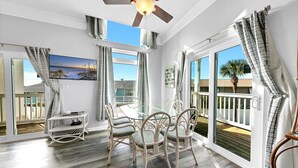 A room with a glass table and chairs, a ceiling fan, and large windows with curtains. - ⭐Beach Across the Street-Pool+Hot Tub-The Palms A6⭐ (Panama City Beach)
