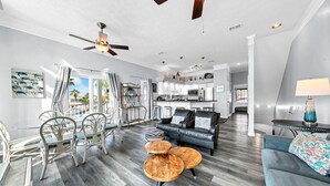 A spacious living area with a modern kitchen, a dining area with wicker chairs, and a balcony with curtains. - ⭐Beach Across the Street-Pool+Hot Tub-The Palms A6⭐ (Panama City Beach)