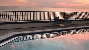 A swimming pool with a view of the sea during sunset.