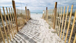 A sandy pathway leading to a beach with wooden fences on either side.