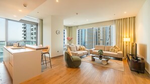 A modern living room with a kitchen area, large windows, and a view of high-rise buildings. - Tranquil 2BR Haven in Heart Dubai Marina (Dubai)