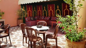 A dining area with a table and chairs, a sofa with patterned cushions, and potted plants. - Riad Jibril (Marrakech)