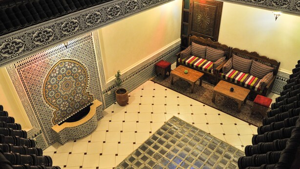 A traditional Moroccan interior with a tiled floor, a patterned wall, a sofa with cushions, and a wooden cabinet. - Riad Jibril (Marrakech)
