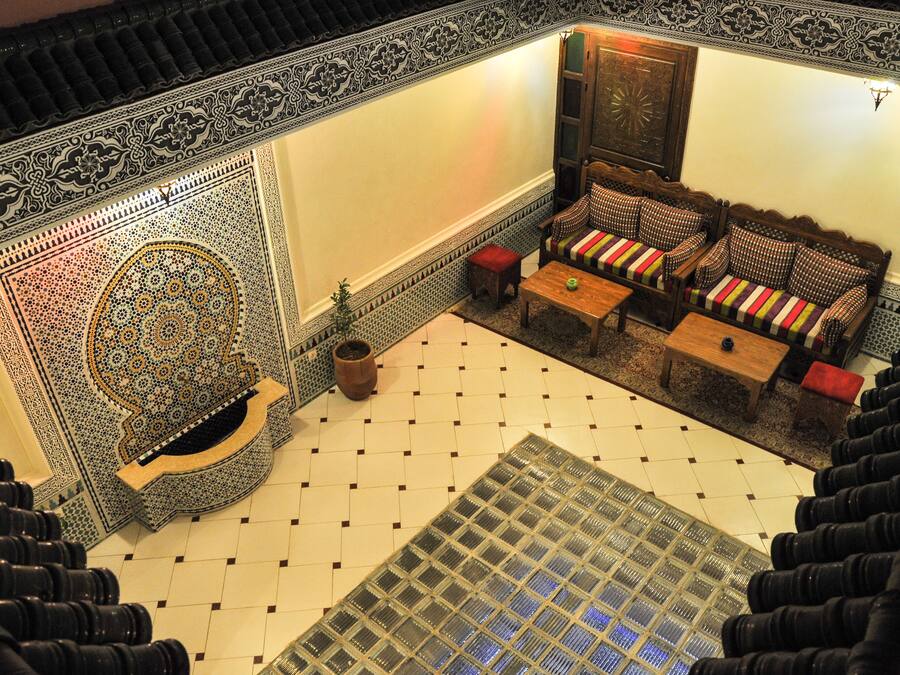 Un interior tradicional marroquí con suelo de mosaicos, pared con diseños, un sofá con cojines y un aparador de madera.