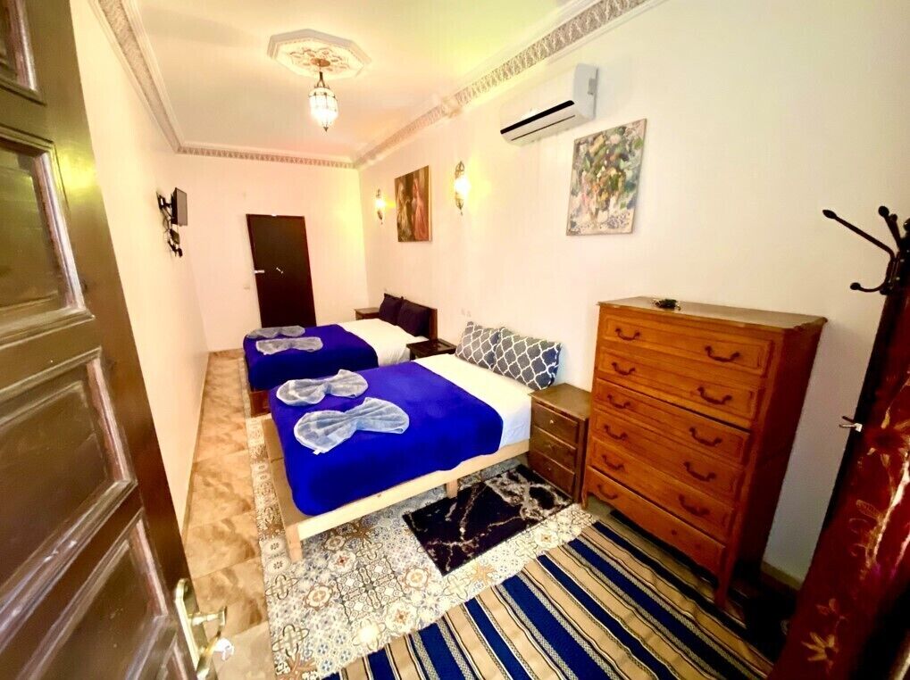 A bedroom with two beds, a wooden dresser, and a patterned rug.