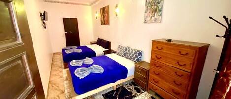 A bedroom with two beds, a wooden dresser, and a patterned rug.