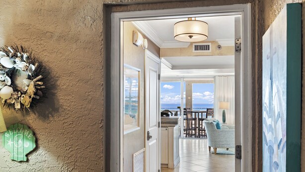A hotel room with a view of the sea, a balcony with outdoor furniture, and a decorative wreath on the wall. - 2BR Penthouse with Panoramic Views + Private Beaches | Magnolia House 602 (Destin)