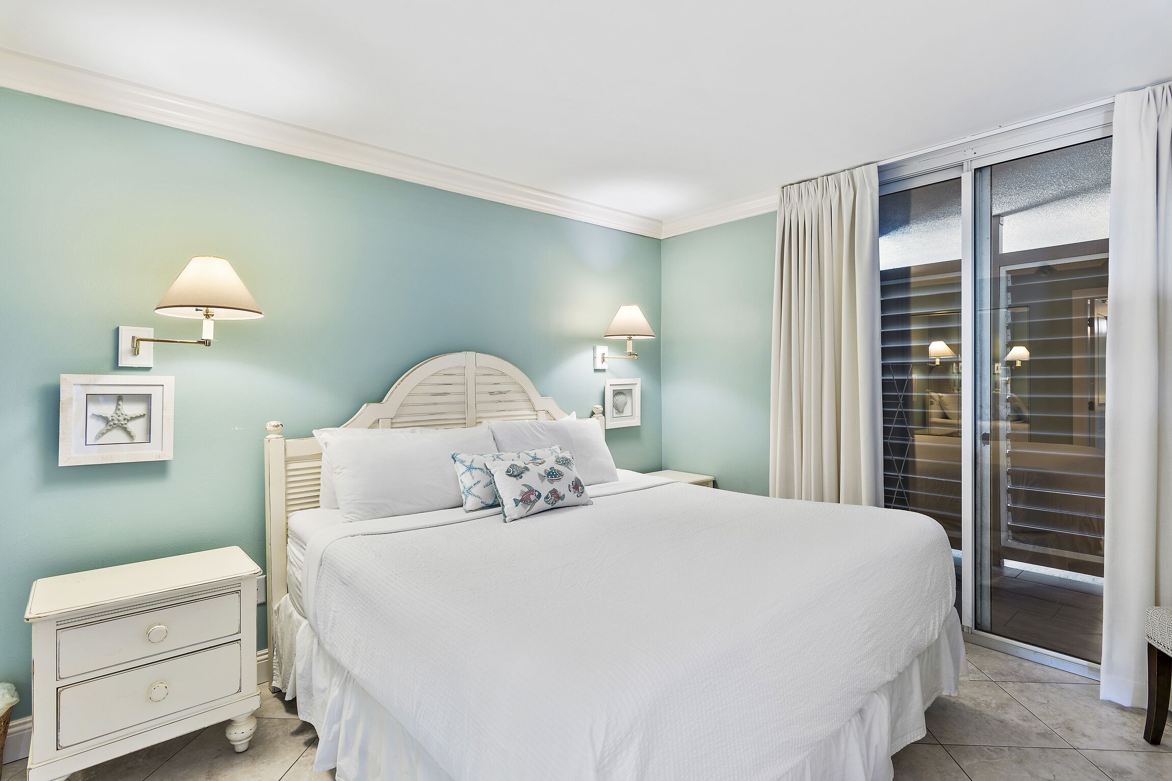 A bedroom with a bed, nightstands, wall-mounted lamps, and a sliding glass door to a balcony.