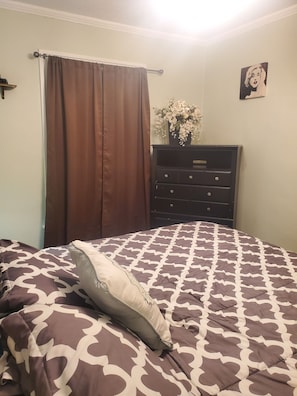 A bedroom with a bed, a dresser, a window with curtains, and a wall with a picture.