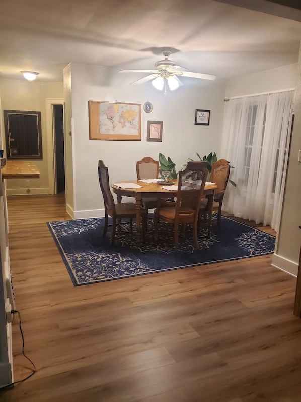 A dining area with a wooden table, chairs, a ceiling fan, and a blue rug.