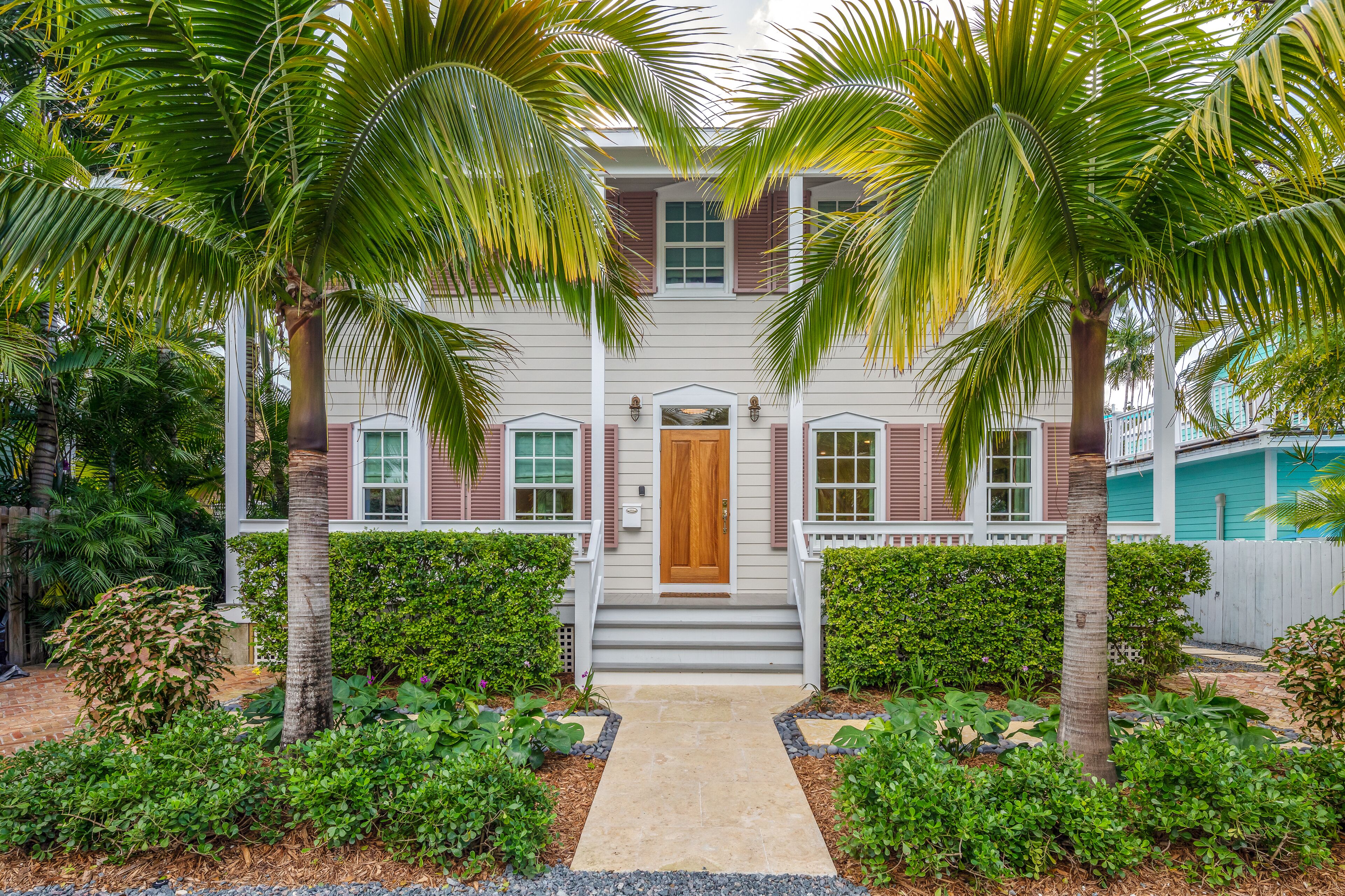 A two-story house with a front porch, a central wooden door, and a pathway leading to the entrance.