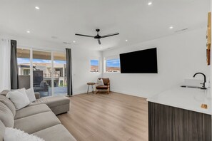 A modern living room with a sofa, a TV mounted on the wall, and a ceiling fan. - Desert Chic at Desert Color by Ember Stays (St. George)