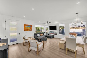 A modern living room with a fireplace, a flat-screen TV, and a dining area with a table and chairs. - Desert Chic at Desert Color by Ember Stays (St. George)