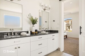 A modern bathroom with a large mirror, dual sinks, and a potted plant.