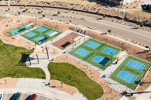 An aerial view of a sports complex with multiple tennis courts, a parking area, and a landscaped area with pathways.