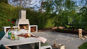 An outdoor patio with a stone table, a pizza oven, and a fire pit.