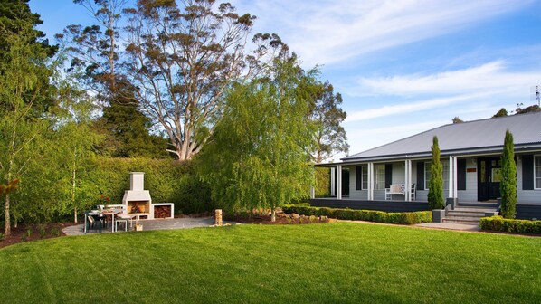 A house with a covered outdoor seating area, a barbecue, and a well-maintained lawn.