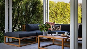 A modern outdoor seating area with a dark-colored sofa and a wooden coffee table, surrounded by lush greenery.