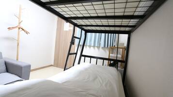 Une petite pièce avec un lit superposé, un canapé gris et un porte-manteau en bois.