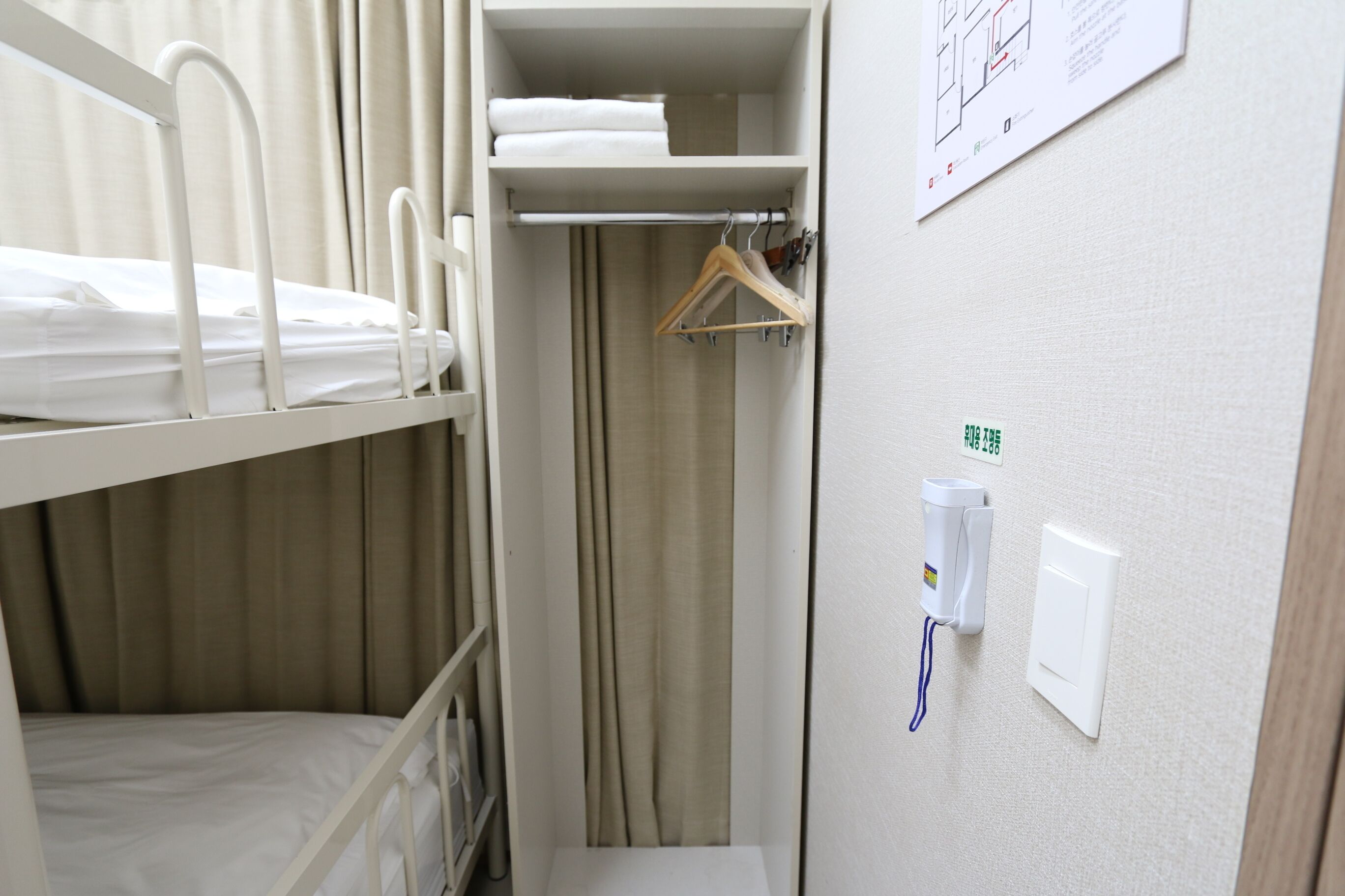 Quarto com beliche, guarda-roupa suspenso, cortina e interruptor de luz na parede.