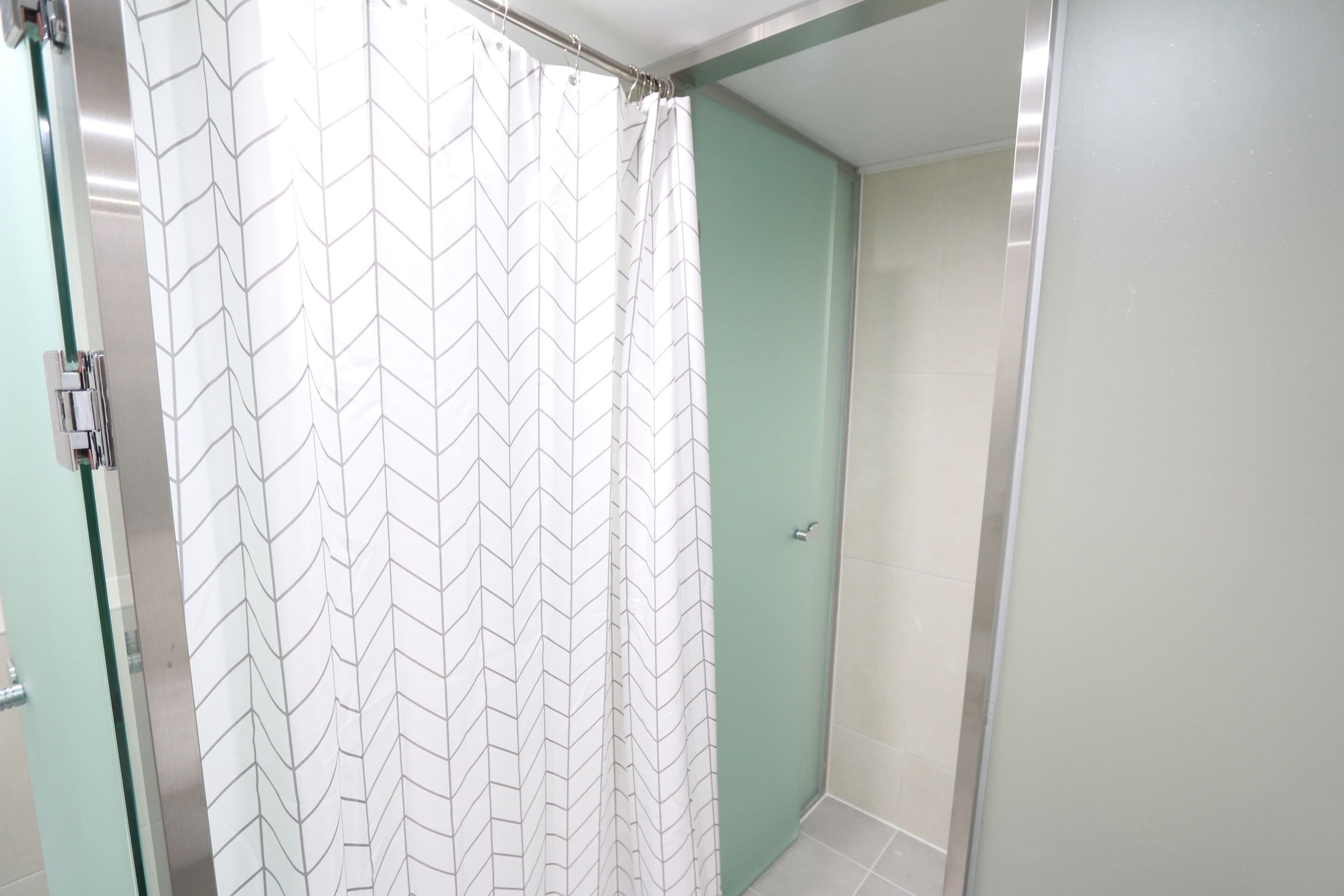 A bathroom with a shower curtain featuring a chevron pattern, a glass shower door, and a green wall.