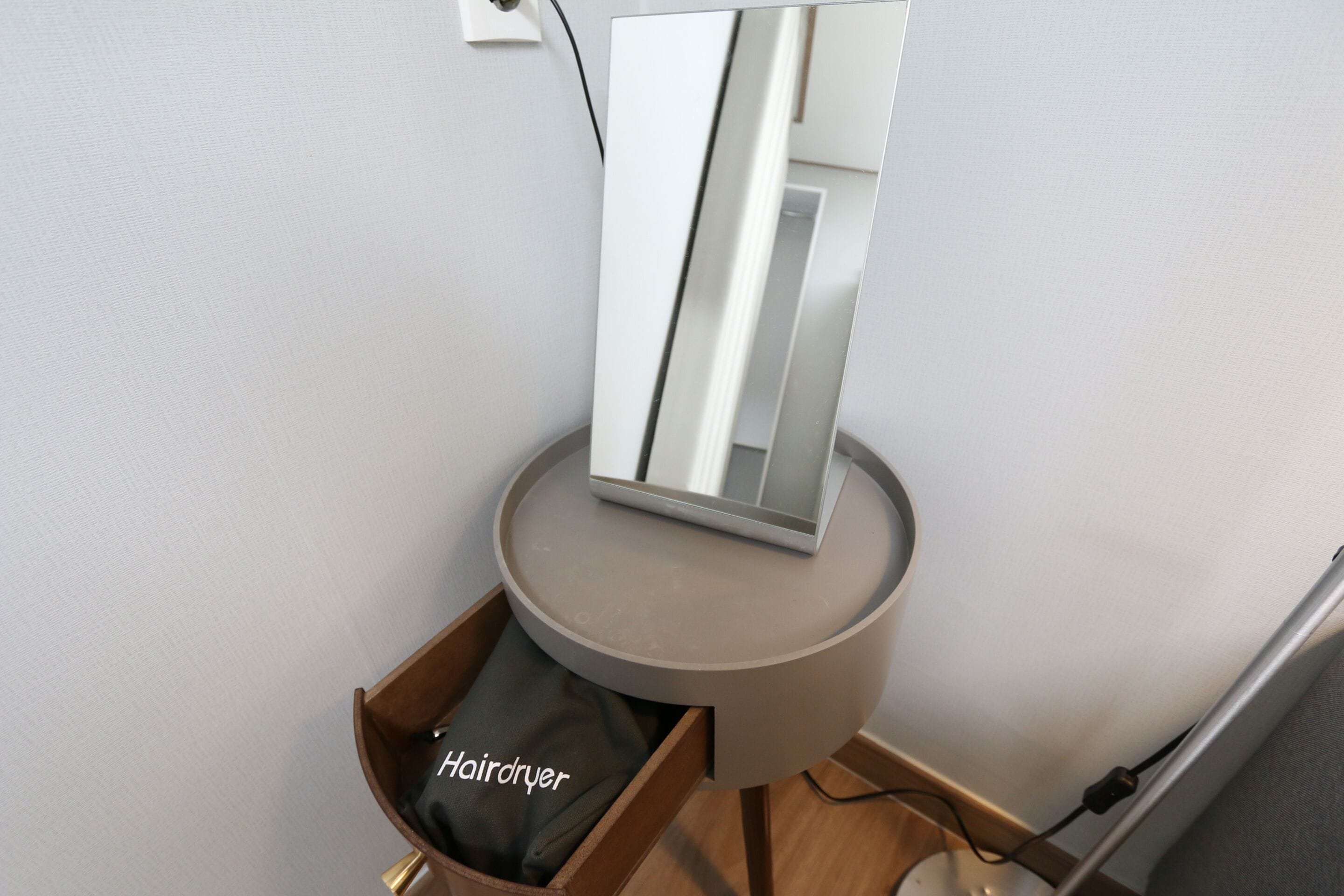 Een moderne badkamer met een haardroger op een houten lade en een spiegel op een rond tafeltje.