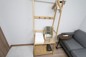 Une pièce de taille modeste, avec un lit superposé en bois, une petite table de chevet, un canapé gris et un miroir fixé au mur.
