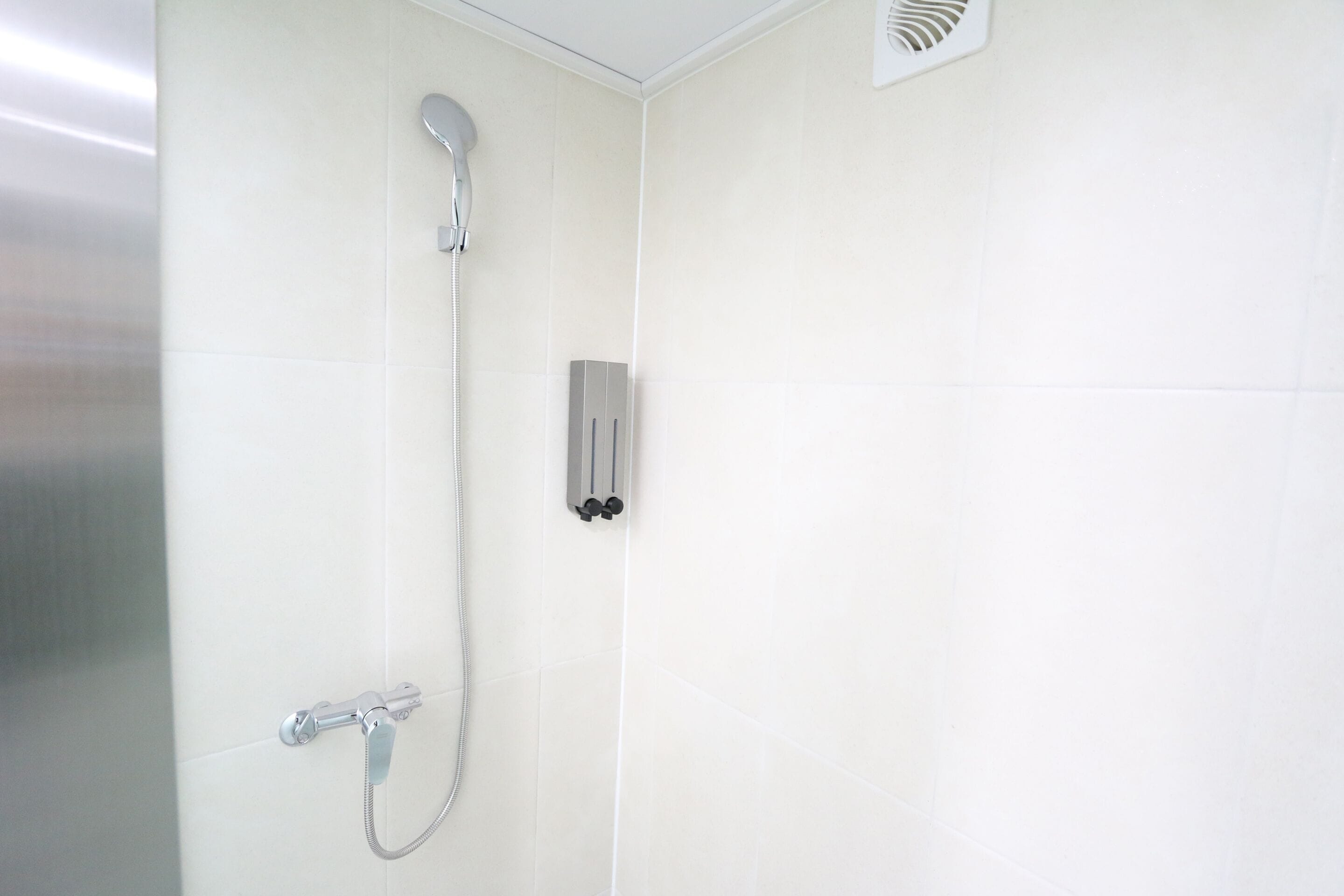 A shower with a handheld showerhead and a wall-mounted control panel.