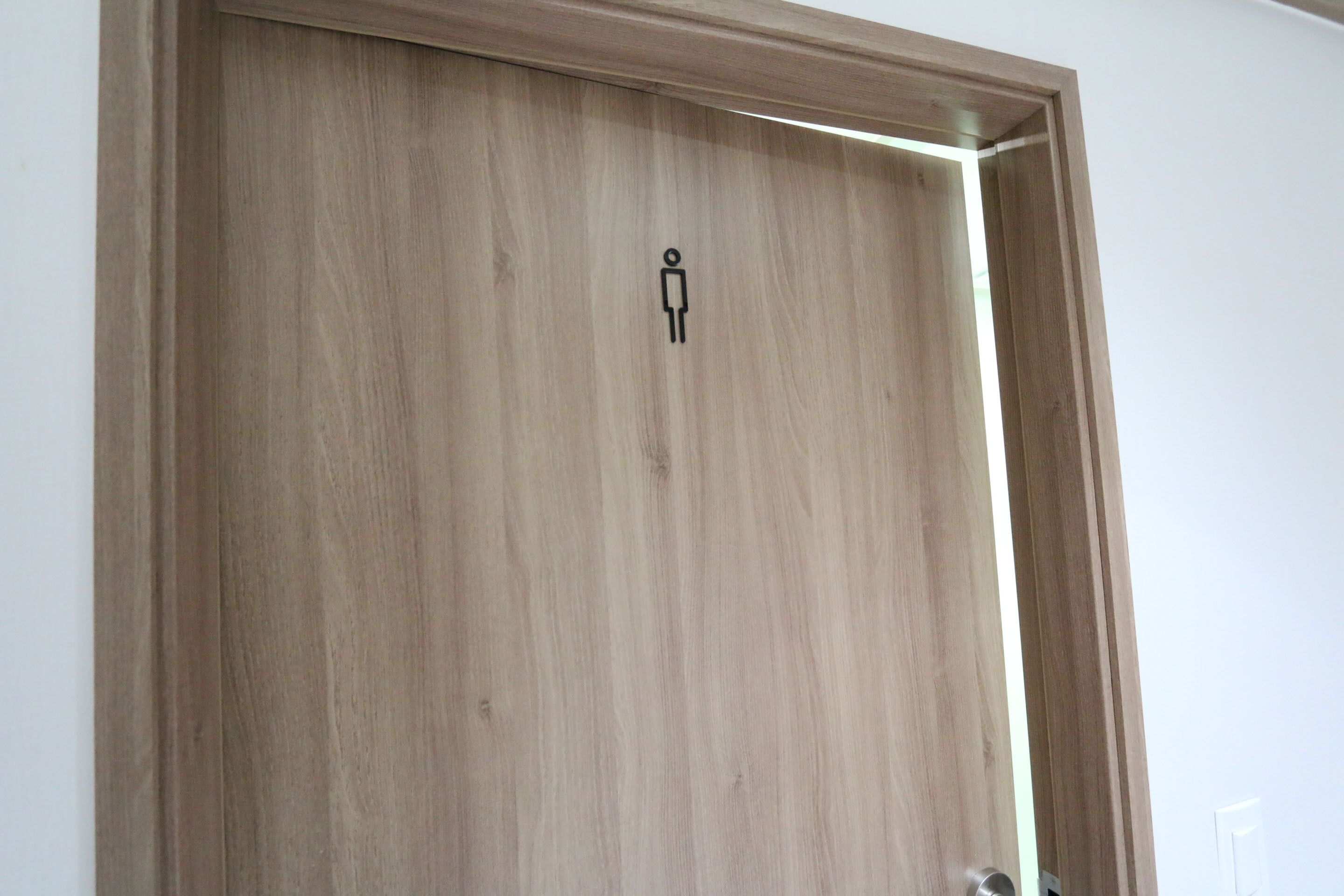 A wooden door with a gender-neutral restroom symbol.